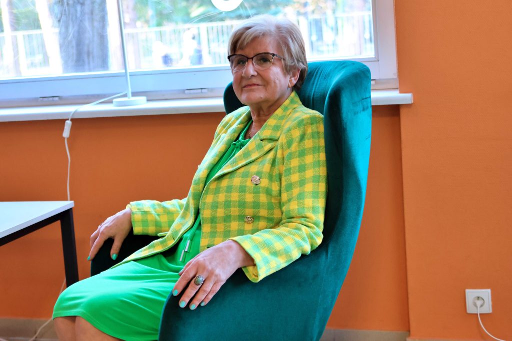 zdjęcie: na fotelu siedzi uśmiechnięta kobieta w odświętnym stroju.