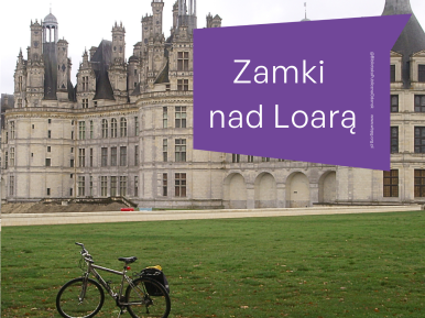 Rower górski wyposażony w sakwy stoi na trawniku przed zamkiem. W tle widać szare niebo.