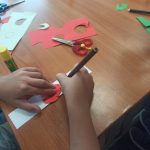 dziecięce ręce kolorujące papierową zakładkę do książki, w tle nożyczki, klej i flamastry