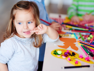 Dziewczynka siedząca przy stole pełnym kolorowych kredek