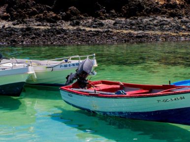Plakat informujący o spotkaniu podróżniczym z Markiem Dąbrowskim. Na plakacie zdjęcie wyspy Fuerteventura - plaży z kolorowymi łodziami