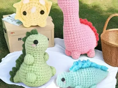 Na obrazku widać 4 maskotki obszyte metodą sztuki amigurami. Są to cztery dinozaury, każdy w innym kolorze: różowy, zielony niebieski oraz żółty.