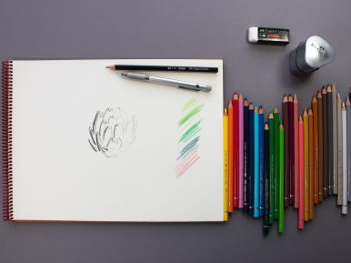 notatnik, kolorowe kredki obok oraz gumka i temperówka