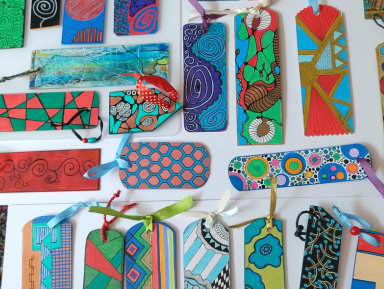 Na obrazku widać dużą ilość kolorowych zakładek do książek pomalowanych techniką neurografiki. Zakładki leżą na białym tle. Każda zakładka ma dołączony kolorowy sznurek.