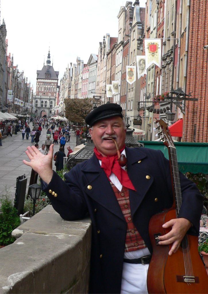 Na fotografii widać artystę, barda Włodzimierza Votkę. Stoi on na ulicy Długiej, na gdańskiej starówce.