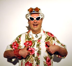 Na zdjęciu uśmiechnięty mężczyzna w kolorowym stroju i okularach.