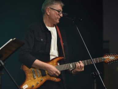 Na zdjęciu widać artystę Bogusława Olszonowicza, który trzyma gitarę elektryczną podczas występu na scenie.