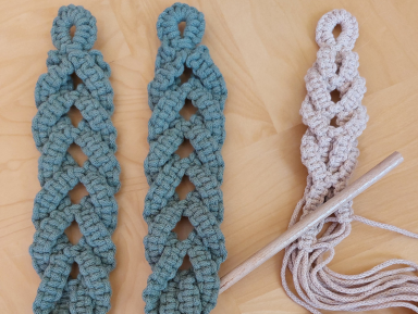 Obrazek przedstawie trzy prace wykonane techniką makramy w kolorze zielonym i beżowym. Tło obrazka jest brązowe.